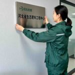 jimeng-2025-11-12-1528-一个穿着墨绿色连帽冲锋衣工装的女士，正在往办公室墙上挂奖牌，牌子是哑光的，左上角...